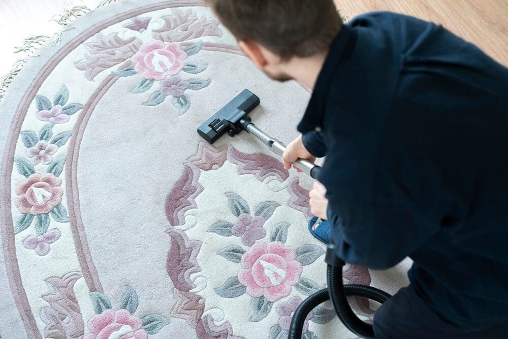A person is vacuuming a patterned area rug with a canister vacuum cleaner.