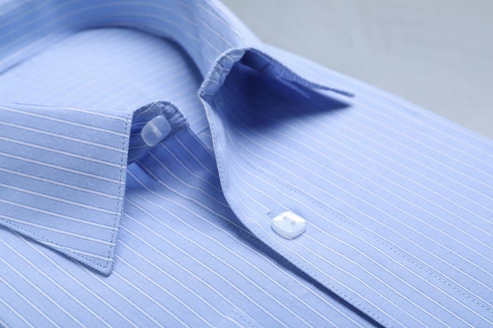 Close-up of a neatly folded light blue dress shirt with thin white vertical stripes and white buttons.