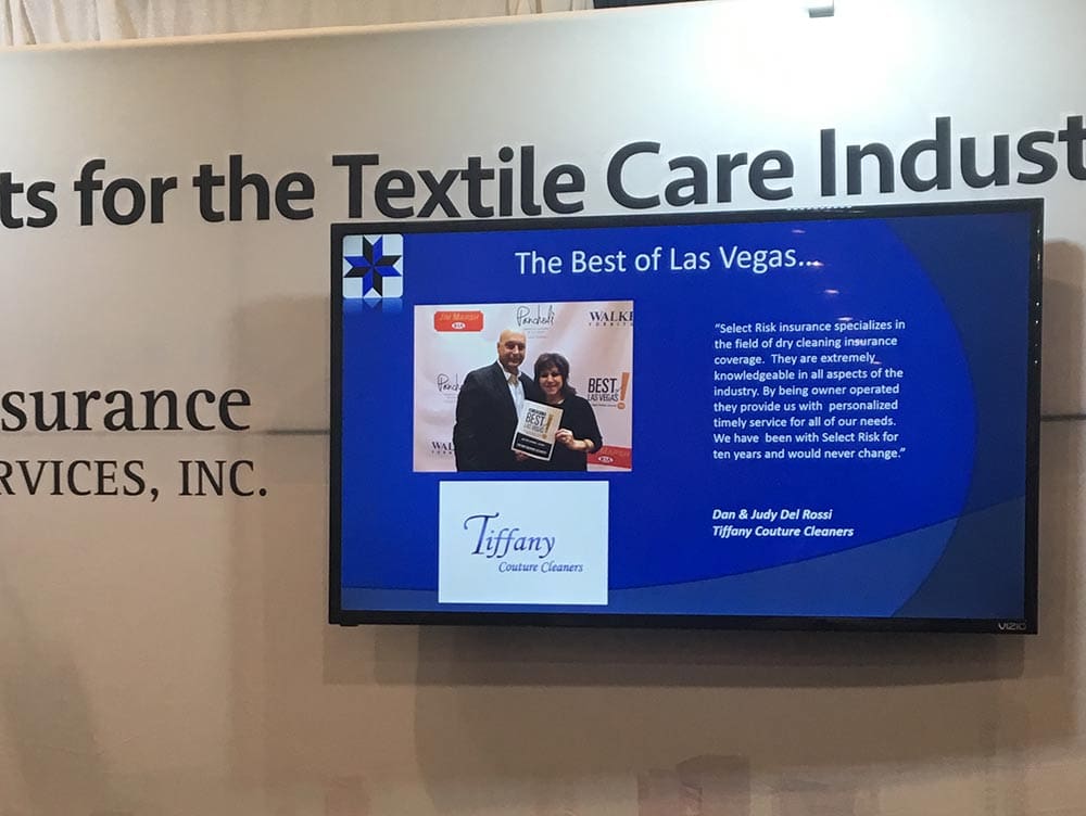 A man and woman stand in front of a presentation screen displaying "The Best of Las Vegas" and "Tiffany Couture Cleaners" at a textile care industry event.
