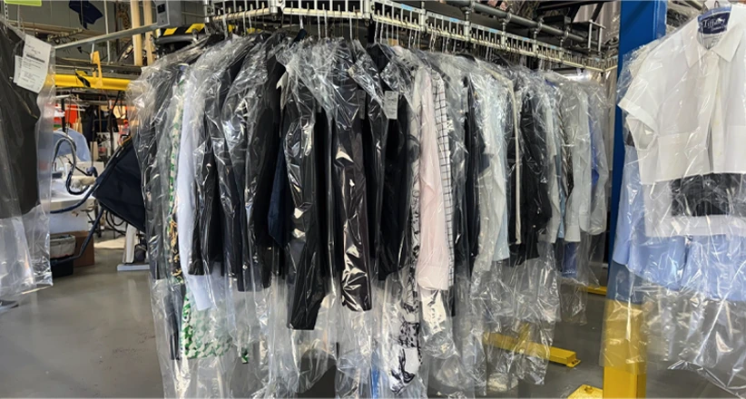 Clothes covered in plastic hang from a conveyor system in a dry cleaning facility.